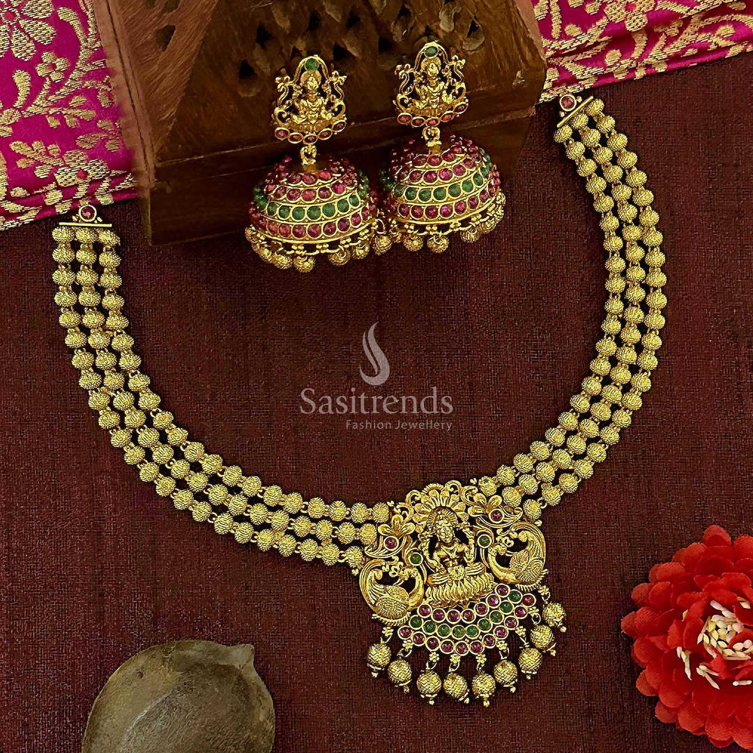 Traditional bridal temple matte gold Lakshmi and peacock necklace set with ruby-green kemp stone pendant and finely detailed jhumkas, ideal for cultural ceremonies and sacred bridal moments – Sasitrends