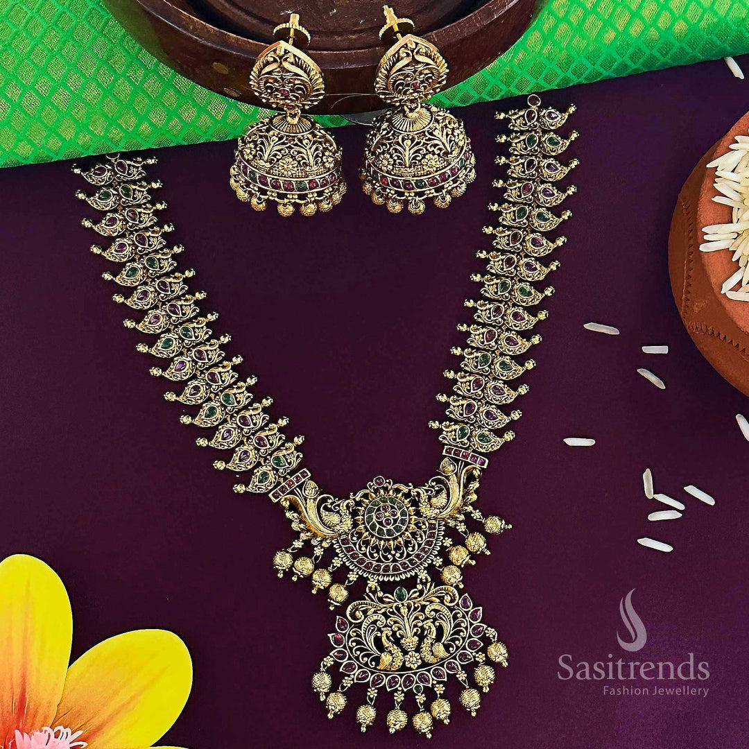 Trendy bridal temple jewellery set in matte gold featuring an ornate peacock floral dual pendant design accentuated with ruby-green stones and delicate jhumkas, ideal for festive grace and ethnic allure – Sasitrends