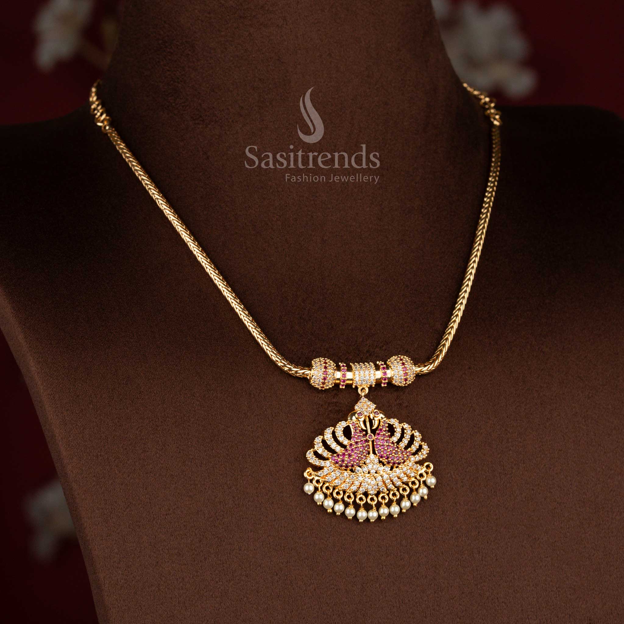 Sasitrends micro gold plated pendant chain necklace designed with a temple-inspired dual peacock pendant structure highlighted by white AD stones and white ruby detailing, perfect for poojas and traditional silk sarees.