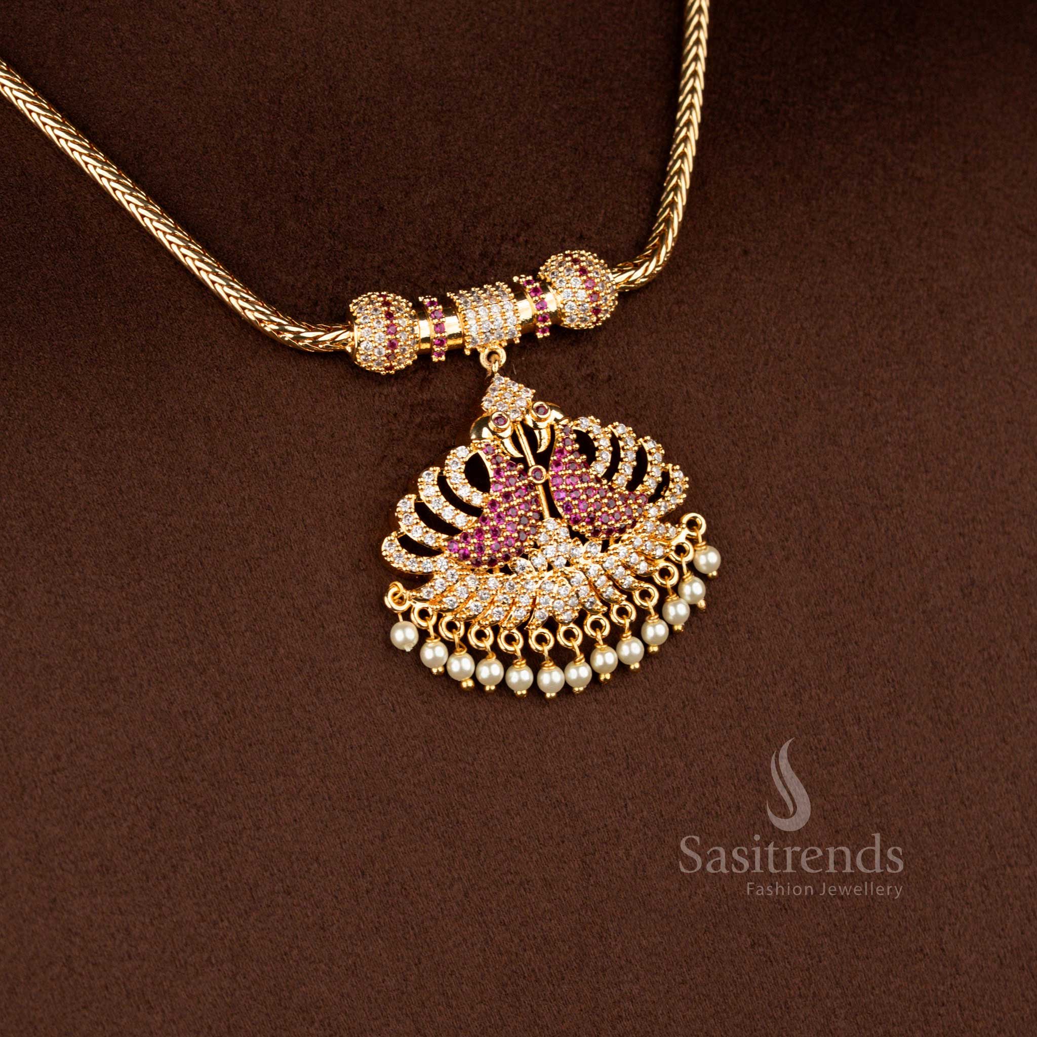 Sasitrends micro gold plated one gram pendant chain necklace crafted with a dual peacock pendant structure accented by white AD stones and white ruby highlights, finished with pearl drops and ideal for temple wear and festive occasions.