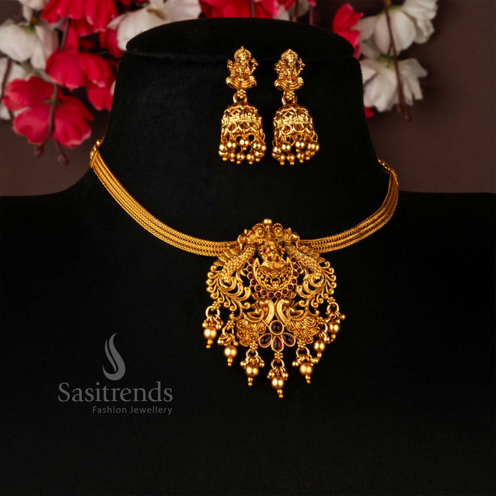 Classic temple matte gold choker jewellery set showcasing an opulent ruby-studded Lakshmi and peacock pendant, paired with matching jhumkas – an exquisite bridal piece celebrating divine grace and timeless tradition – Sasitrends