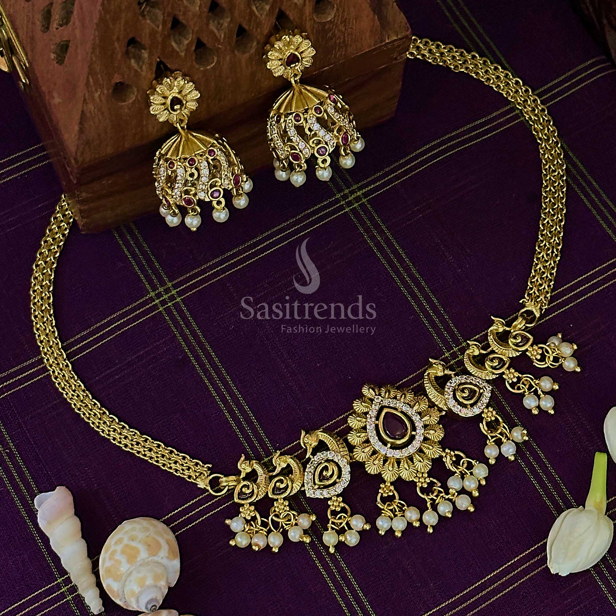 Striking ruby-white choker necklace in matte gold finish, enhanced with peacock charm, glimmering AD stones, and ornate jhumkas – ideal for bridal elegance – Sasitrends