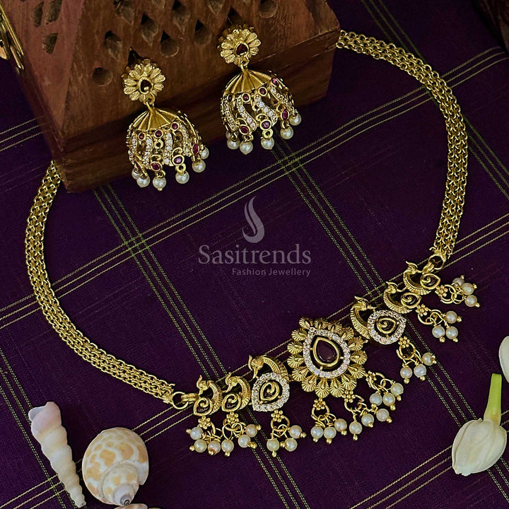 Striking ruby-white choker necklace in matte gold finish, enhanced with peacock charm, glimmering AD stones, and ornate jhumkas – ideal for bridal elegance – Sasitrends