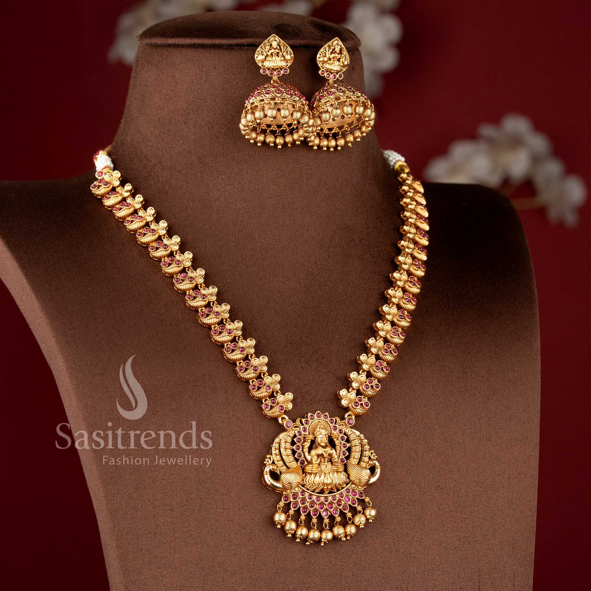 Heavy bridal temple matte gold haram necklace with detailed Lakshmi and peacock design in ruby color, paired with matching jhumkas by Sasitrends for festive look