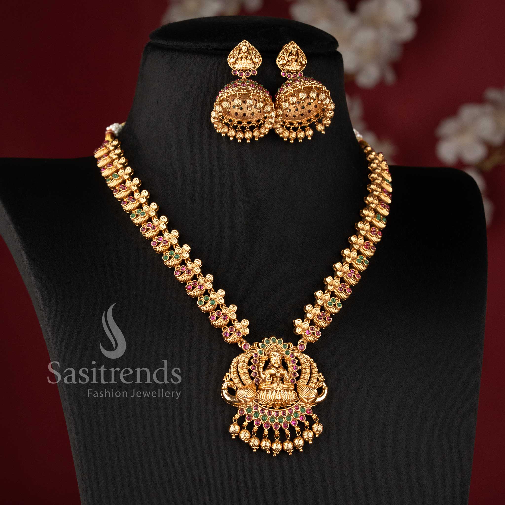 Heavy bridal temple matte gold haram necklace with detailed Lakshmi and peacock design in ruby color, paired with matching jhumkas by Sasitrends for festive look
