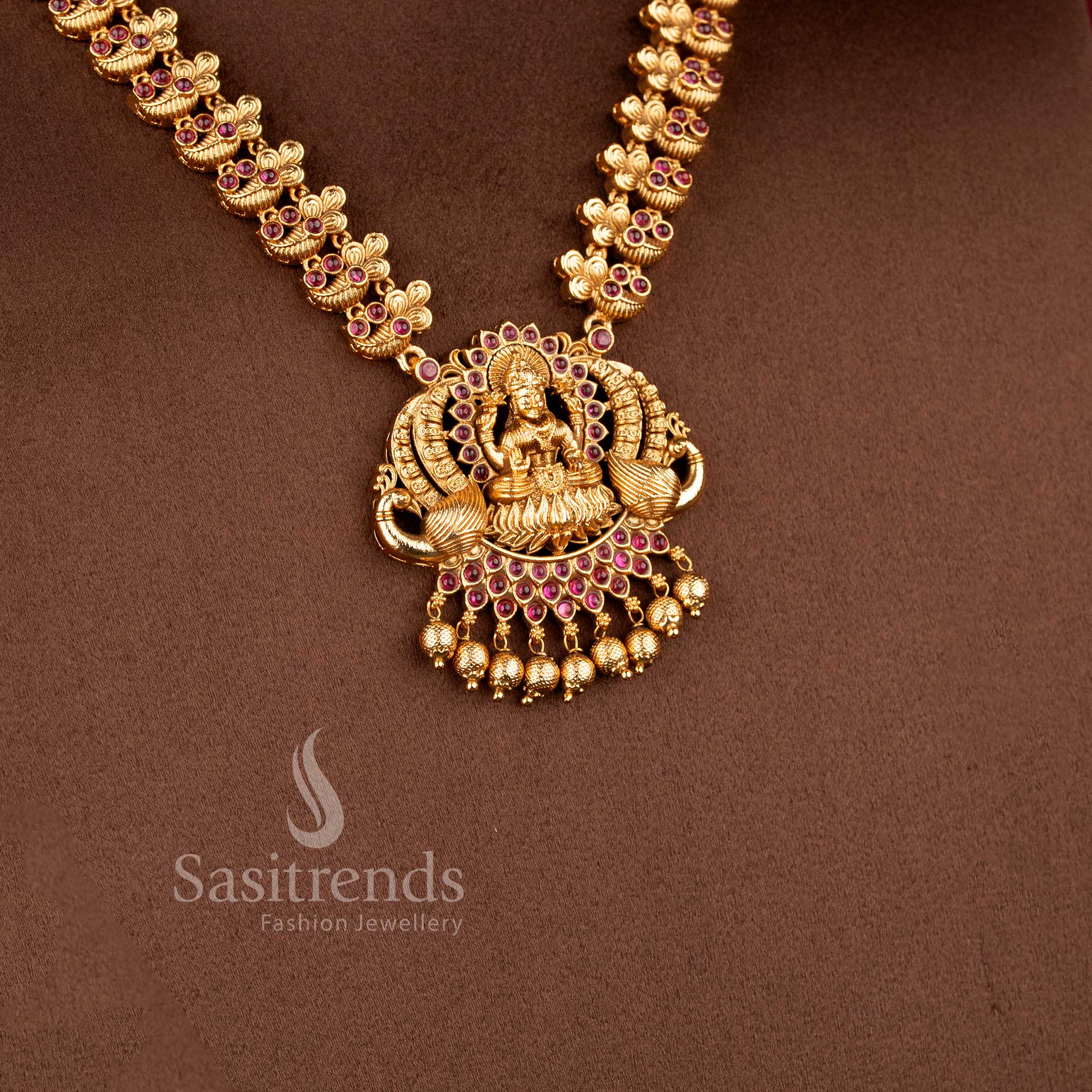 Traditional bridal wear temple matte gold tone Lakshmi and peacock haram necklace jewellery set in ruby green color with matching jhumkas by Sasitrends, perfect for wedding and festive occasions