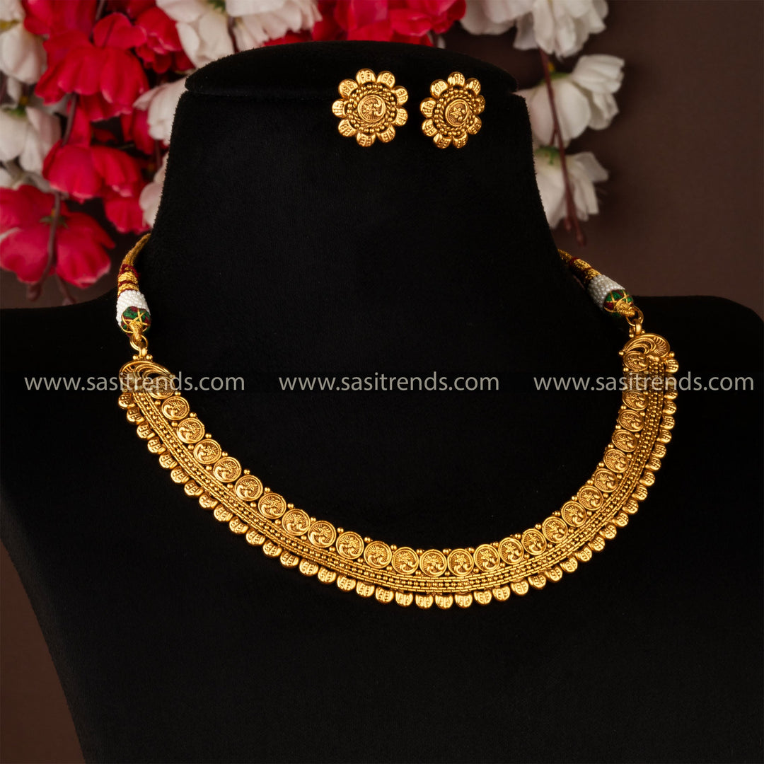 Antique gold-plated brass necklace and earrings set with traditional floral design on a black display stand