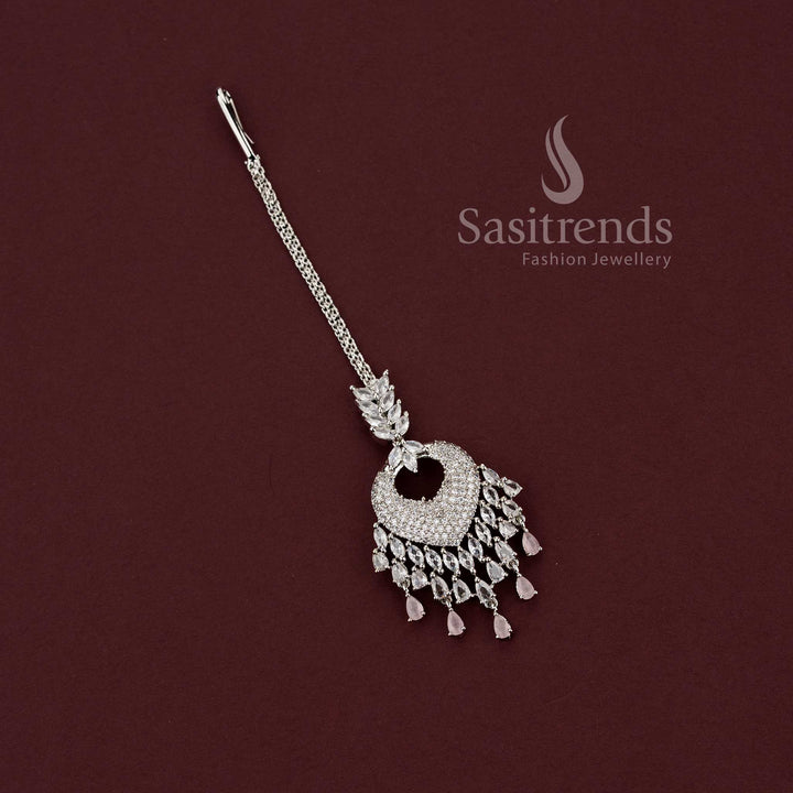Romantic bridal rhodium silver maang tikka 2129F featuring a heart-shaped American Diamond pendant and delicate pink stone dangling drops, perfect for wedding lehengas and engagement ceremony look