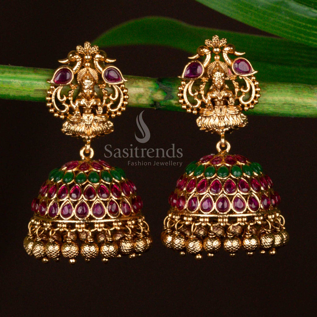 Matte gold plated temple-style jhumka earrings featuring peacock and Lakshmi motifs in a stunning ruby-green combination, ideal for exquisite bridal and festive traditional wear – sasitrends