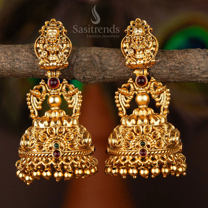 Traditional matte gold jhumkas adorned with antique ruby-green  stones, Lakshmi figurework and classic South Indian drum-style drop design, perfect for ethnic bridal wear – Sasitrends