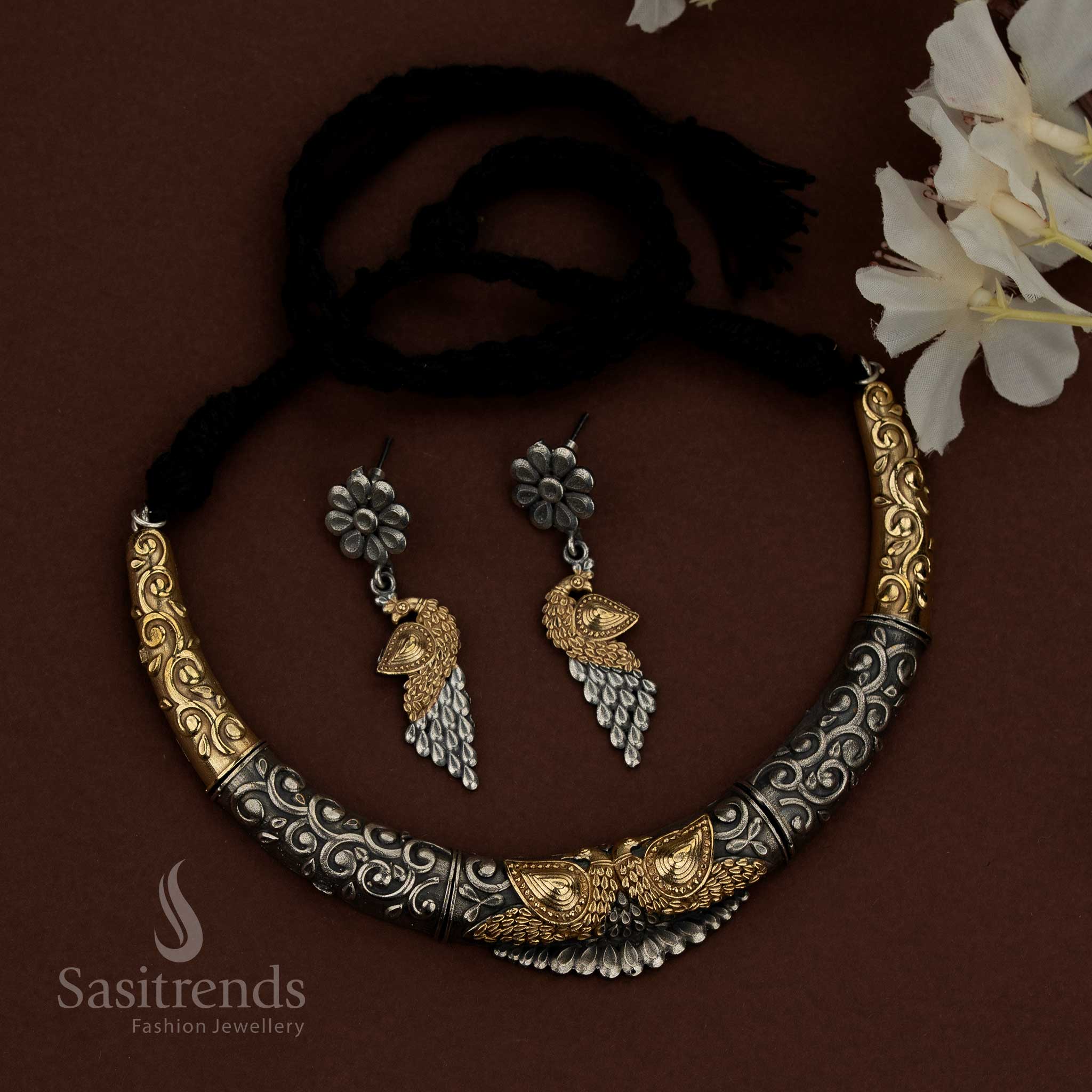 Sasitrends 92.5 dual tone silver oxidised husli jewellery set featuring a bold crescent necklace design with engraved scrollwork patterns, raised floral embossed elements, central peacock motif detailing, structured surface finish, traditional thread fastening, and matching earrings designed with floral studs and layered peacock-inspired drops for ethnic heritage wear.