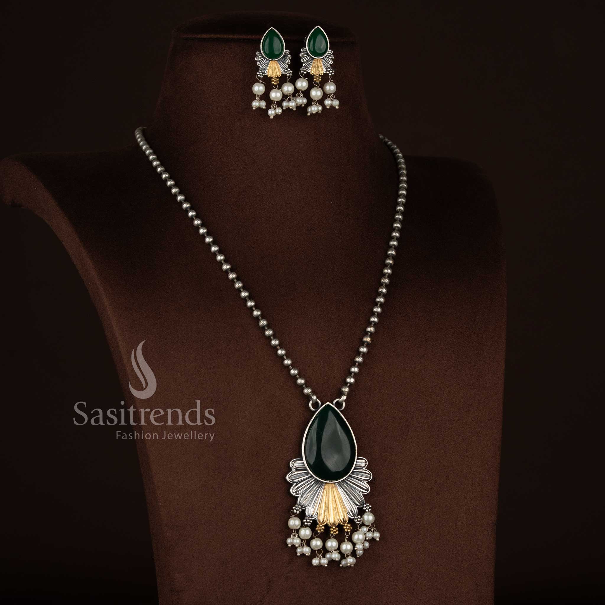 
Antique oxidised 92.5 silver plated Monalisa stone necklace set in green shade, featuring a structured floral drop pendant, intricate layered silver textures, subtle gold accents, pearl bead hangings, oxidised beaded chain, and coordinated floral earrings
