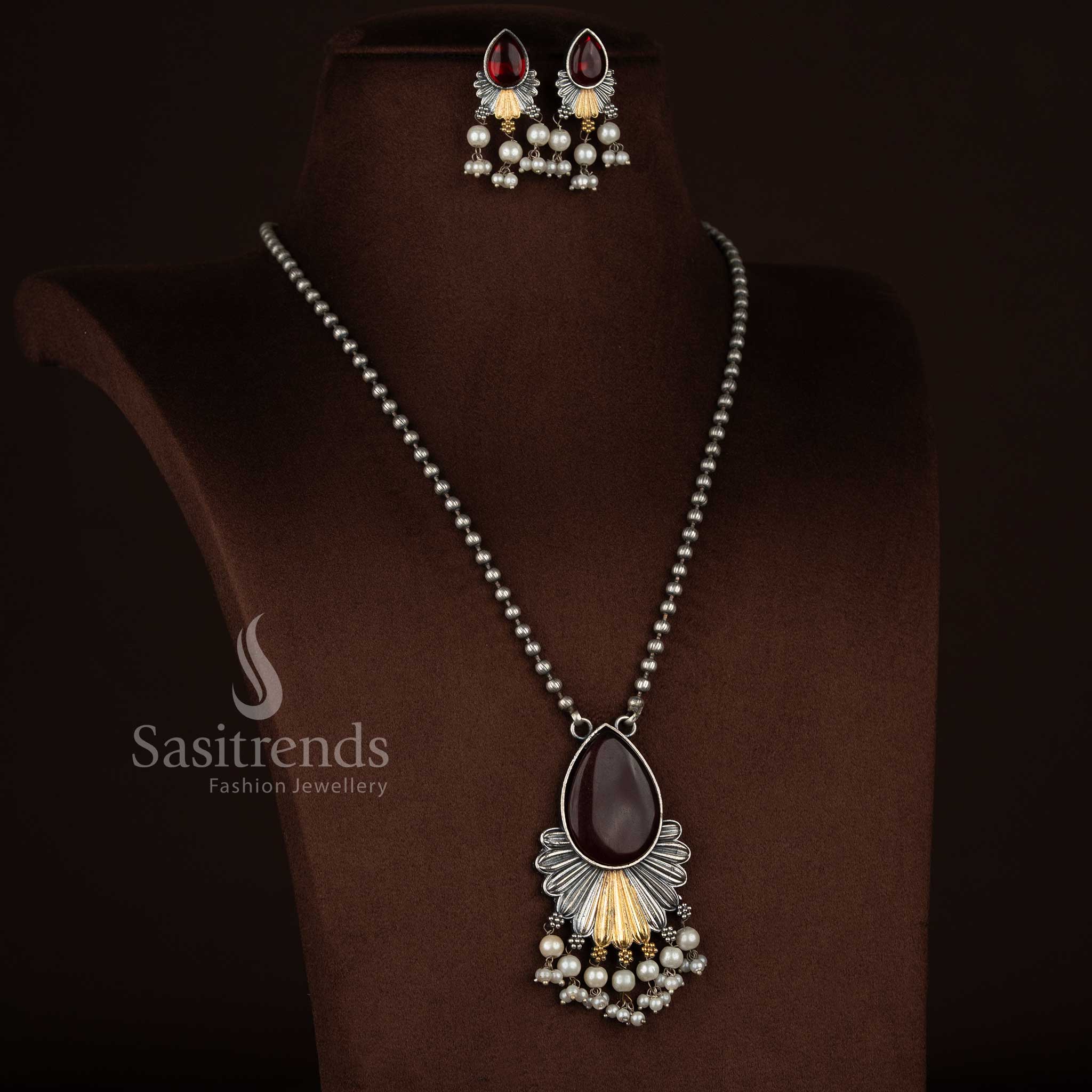 
Antique oxidised 92.5 silver plated Monalisa stone necklace jewellery set in red shade, featuring a teardrop floral layered drop pendant with fan-style silver structure, gold tone accents, pearl bead hangings, oxidised beaded chain, and matching floral earrings with pearl detailing
