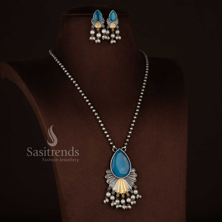 
Antique oxidised 92.5 silver plated Monalisa stone necklace set in sky blue tone, designed with a structured teardrop pendant, layered floral silver work, subtle gold highlights, cascading pearl bead danglers, oxidised beaded chain, and coordinated floral drop earrings - Sasitrends
