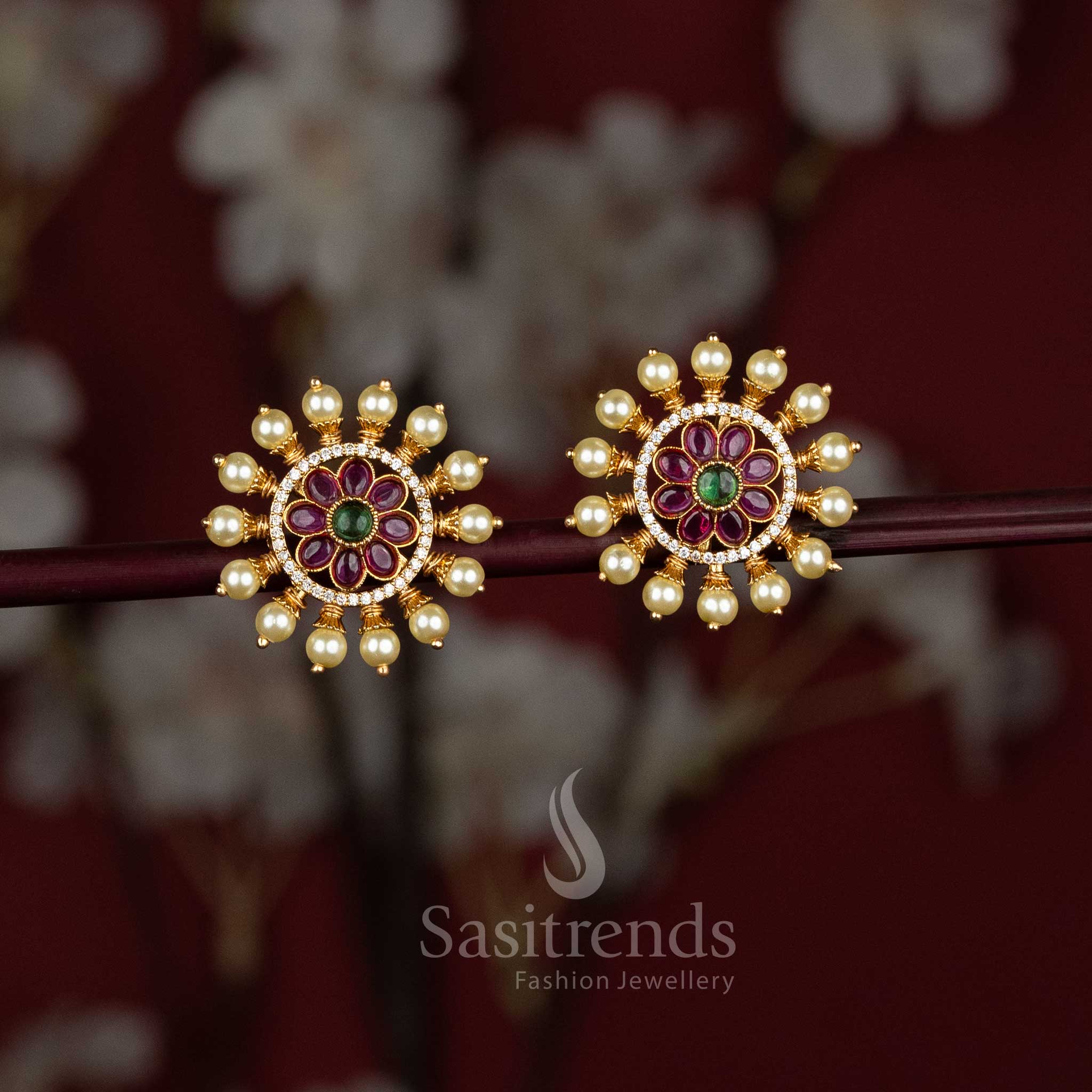 Elegant ruby-multi floral stud earrings in matte gold finish, highlighted with sparkling AD stones and graceful pearl edging – ideal for cultural and occasional jewellery styling from Sasitrends