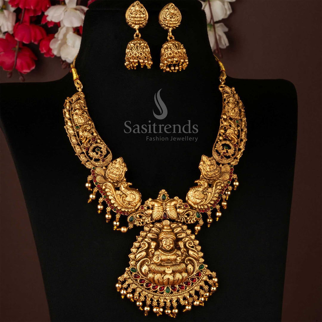 Classic matte gold plated Lakshmi and peacock motif pendant necklace set paired with grand traditional jhumka earrings – an exquisite temple jewellery creation ideal for bridal and festive wear ensembles – Sasitrends