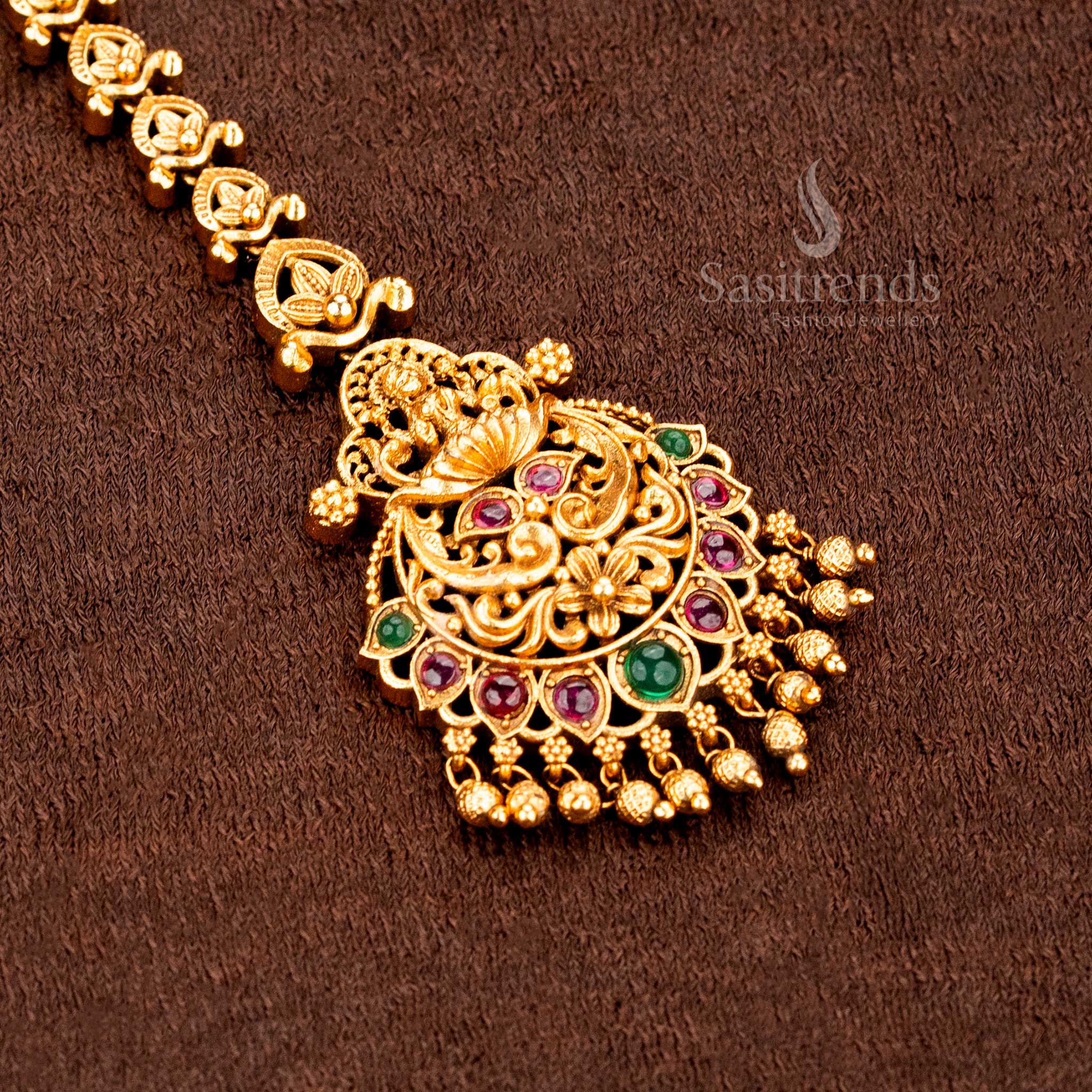 Temple matte gold plated Lakshmi peacock mango floral tikka adorned with AD stones and hanging balls, crafted for bridal brilliance and traditional jewellery glory -sasitrends