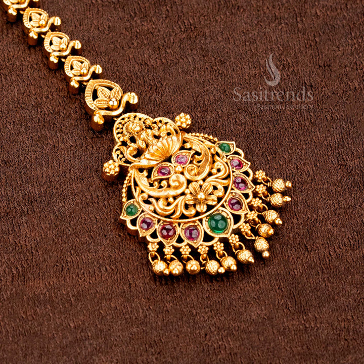 Temple matte gold plated Lakshmi peacock mango floral tikka adorned with AD stones and hanging balls, crafted for bridal brilliance and traditional jewellery glory -sasitrends