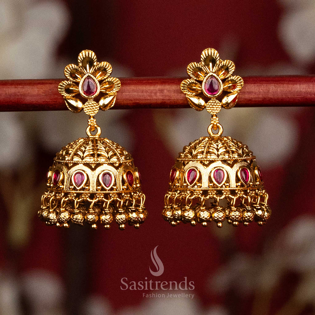 Elegant temple style matte gold jhumka earrings designed with ruby accents, layered floral petal motifs, sculpted teardrop dome and traditional gold bead drops for festive cultural wear - Sasitrends