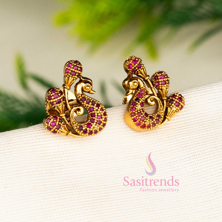 Graceful matte gold ruby peacock stud earrings adorned with rich kemp American diamond stones and temple-inspired floral designs for a timeless festive look by Sasitrends.