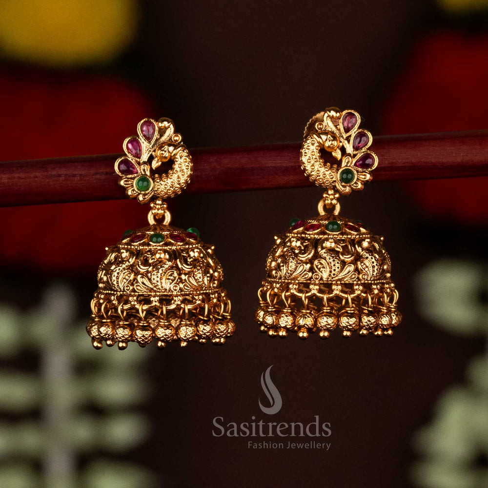 Graceful ruby-green temple matte gold plated royal peacock jhumka earrings adorned with ghungroo charm drops, ideal for traditional occasions and festive saree ensembles by Sasitrends