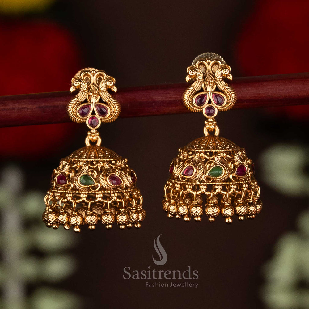 Stunning ruby-green matte gold plated temple peacock jhumka earrings enhanced with ghungroo drops, designed for grand festive saree wear and ethnic glamour by Sasitrends