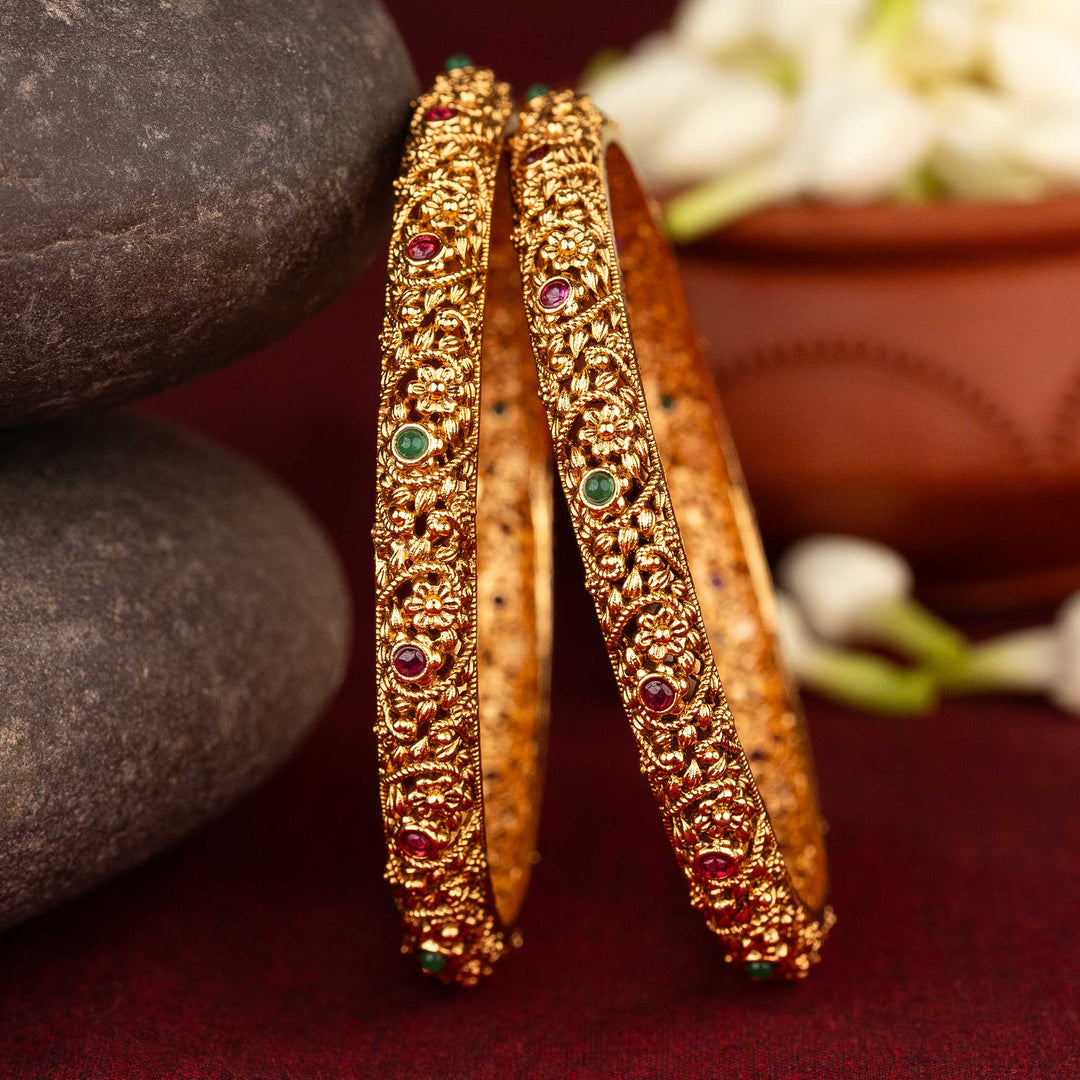 Antique matte gold bangles with intricate floral motifs and green AD stones