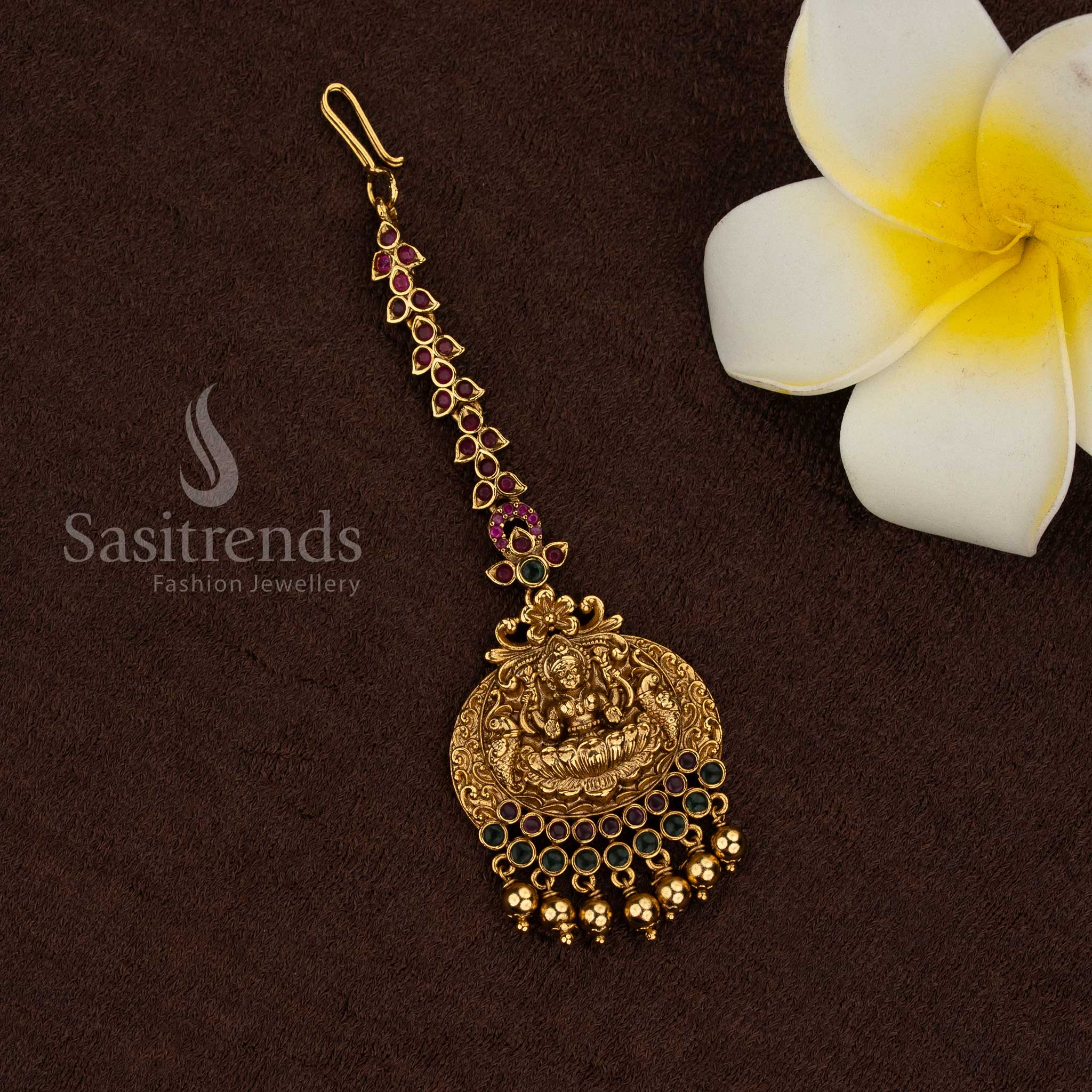 
Traditional temple matte gold plated circular Lakshmi medallion maang tikka with ruby green stone border and bead drops, premium quality jewellery for bridal and festive wear - Sasitrends
