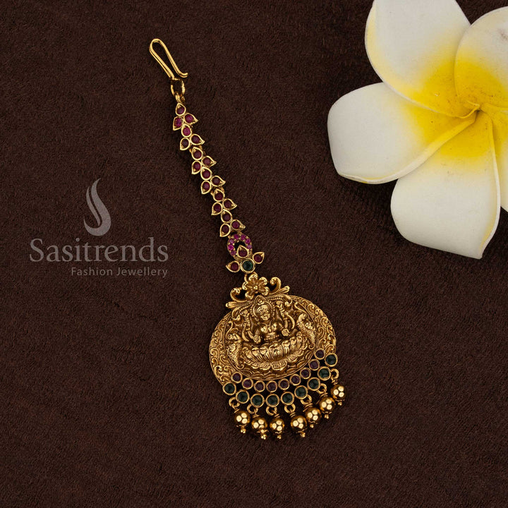 
Traditional temple matte gold plated circular Lakshmi medallion maang tikka with ruby green stone border and bead drops, premium quality jewellery for bridal and festive wear - Sasitrends
