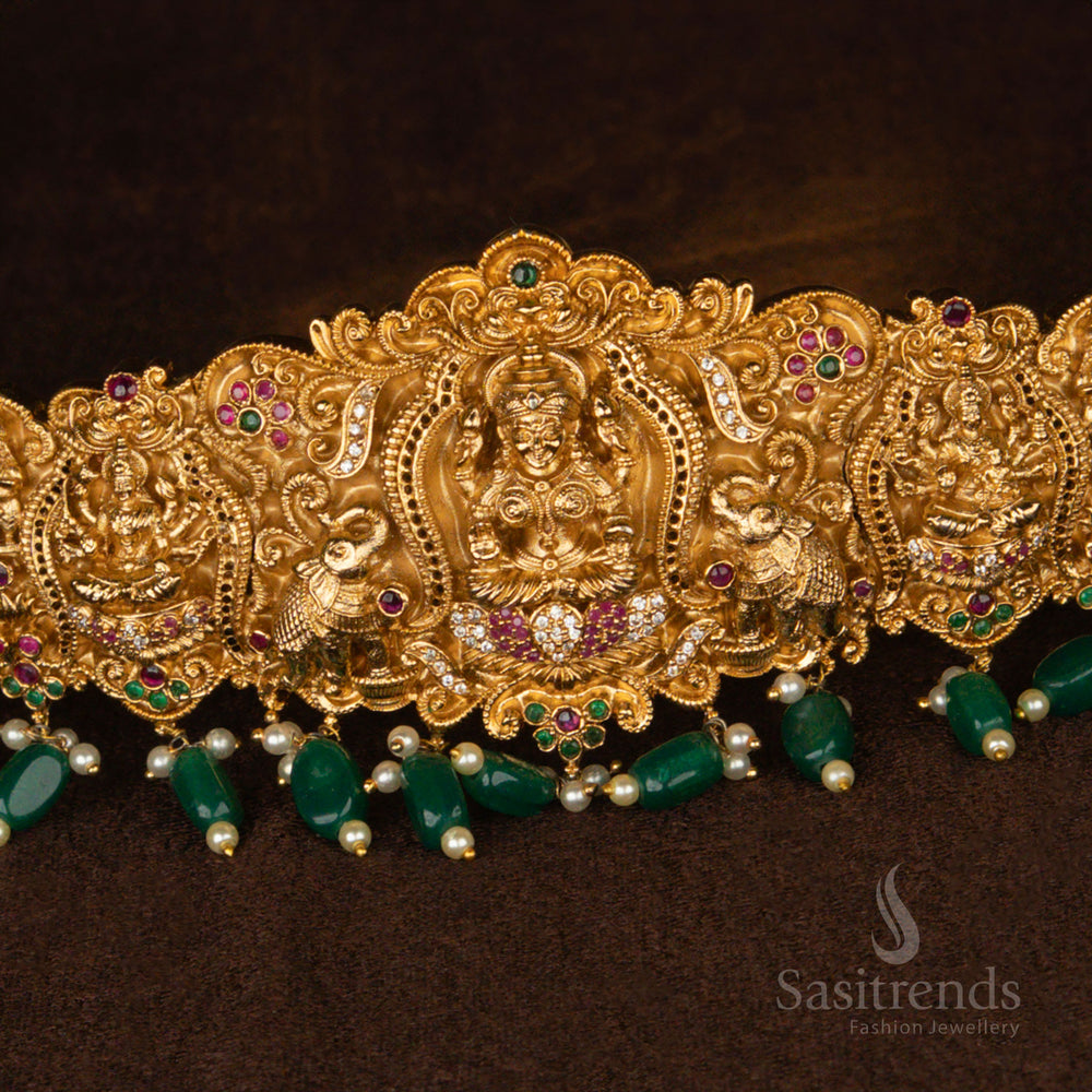 Grand bridal waist belt in matte gold plating with a divine Lakshmi centerpiece, beautifully decorated with peacock and elephant detailing and shimmering green pearl hangings - Sasitrends