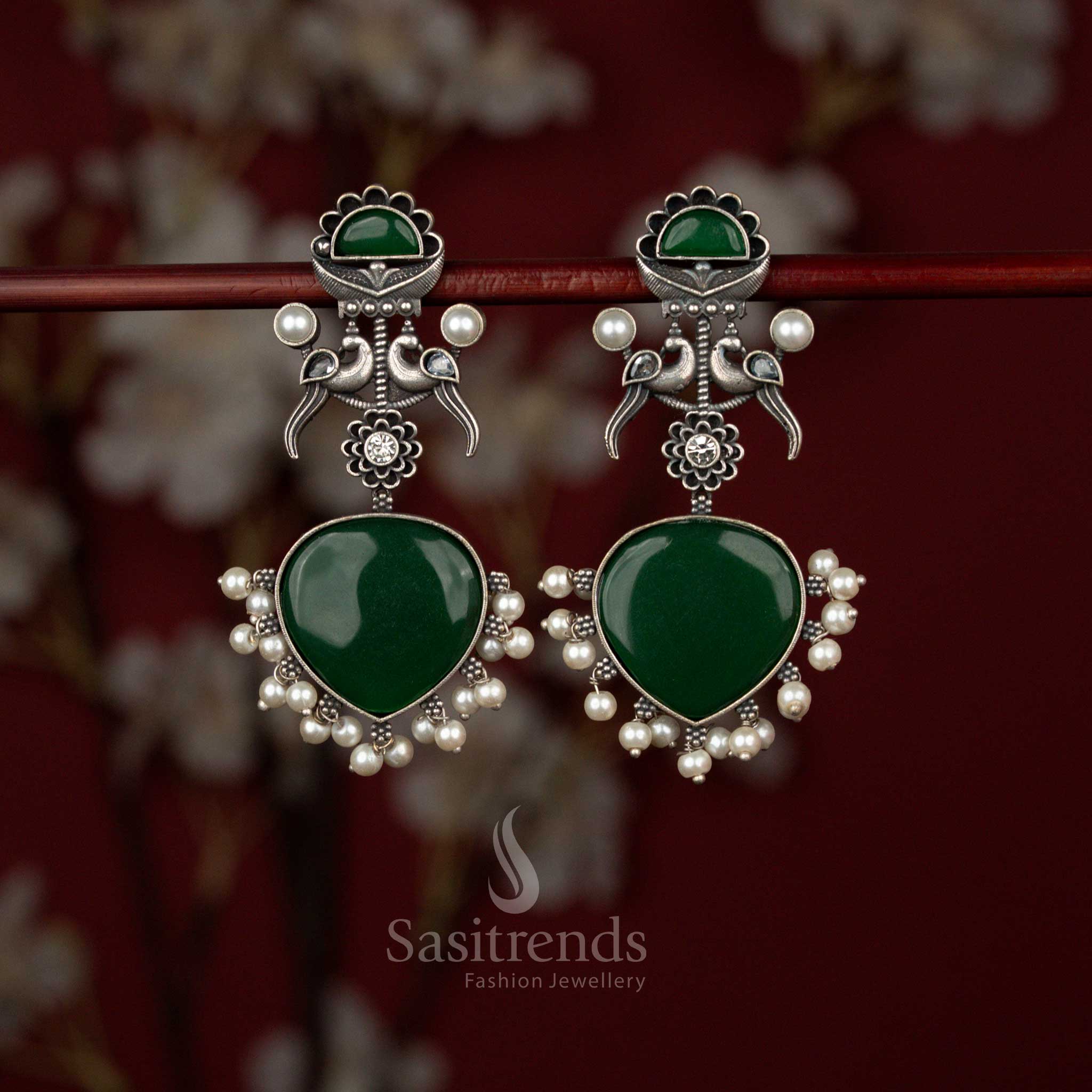 Sasitrends green oxidised German silver heart-shaped earrings featuring dual peacock motifs, intricate detailing and delicate pearl hangings, perfect for festive dressing and traditional celebrations.