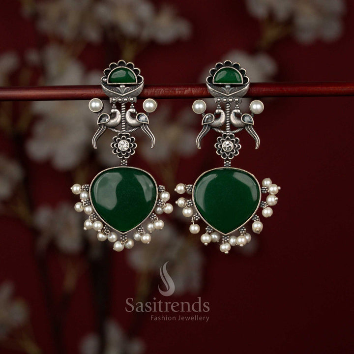 Sasitrends green oxidised German silver heart-shaped earrings featuring dual peacock motifs, intricate detailing and delicate pearl hangings, perfect for festive dressing and traditional celebrations.