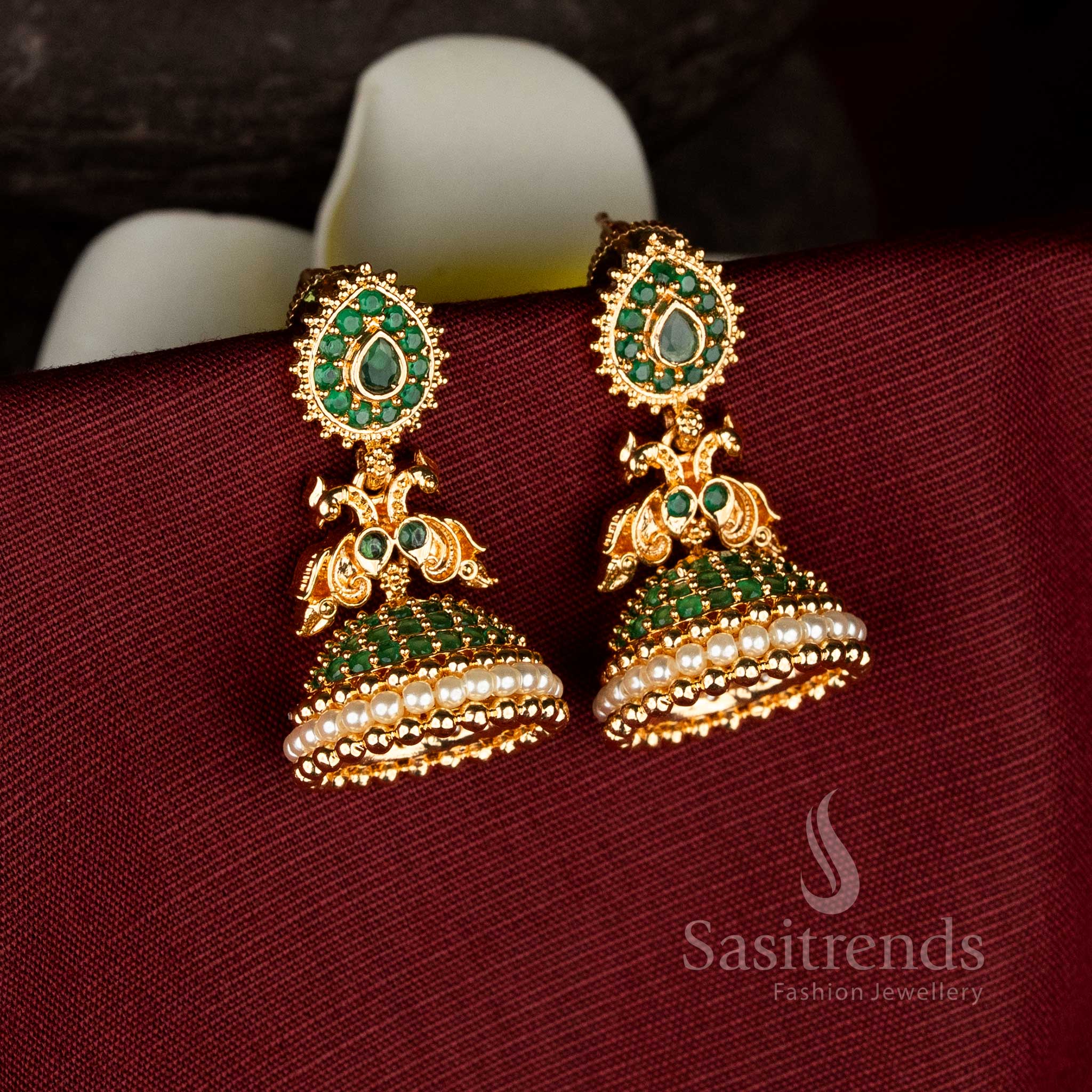 Micro gold plated jhumka earrings from Sasitrends featuring teardrop motif green American diamond stud, dual peacock carved structure, and pearl layered dome design