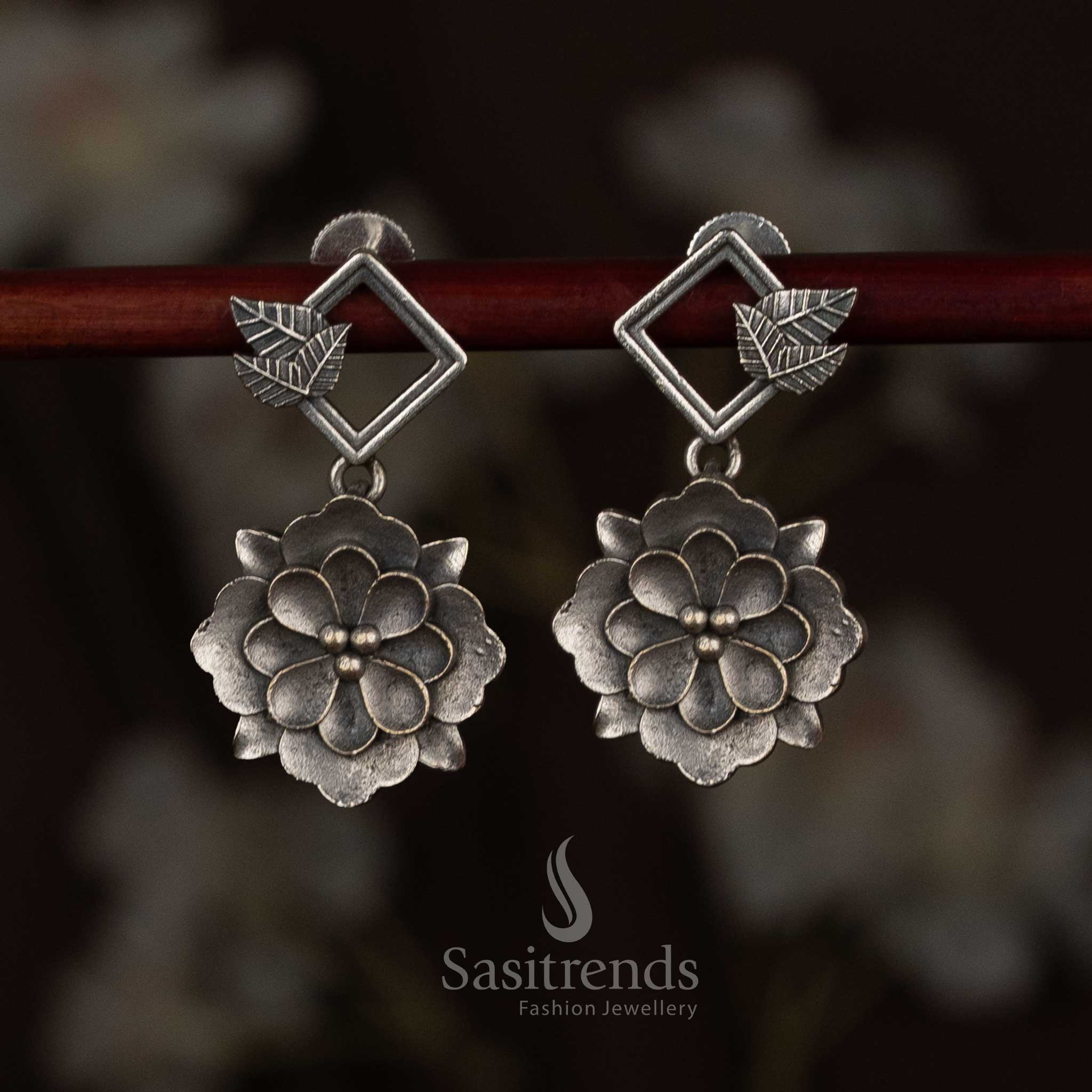 Sasitrends antique oxidised 92.5 silver plated earrings featuring a geometric diamond-shaped top connected to a layered floral drop motif with sculpted petal detailing, heritage-inspired silver finish, and elegant ethnic design
