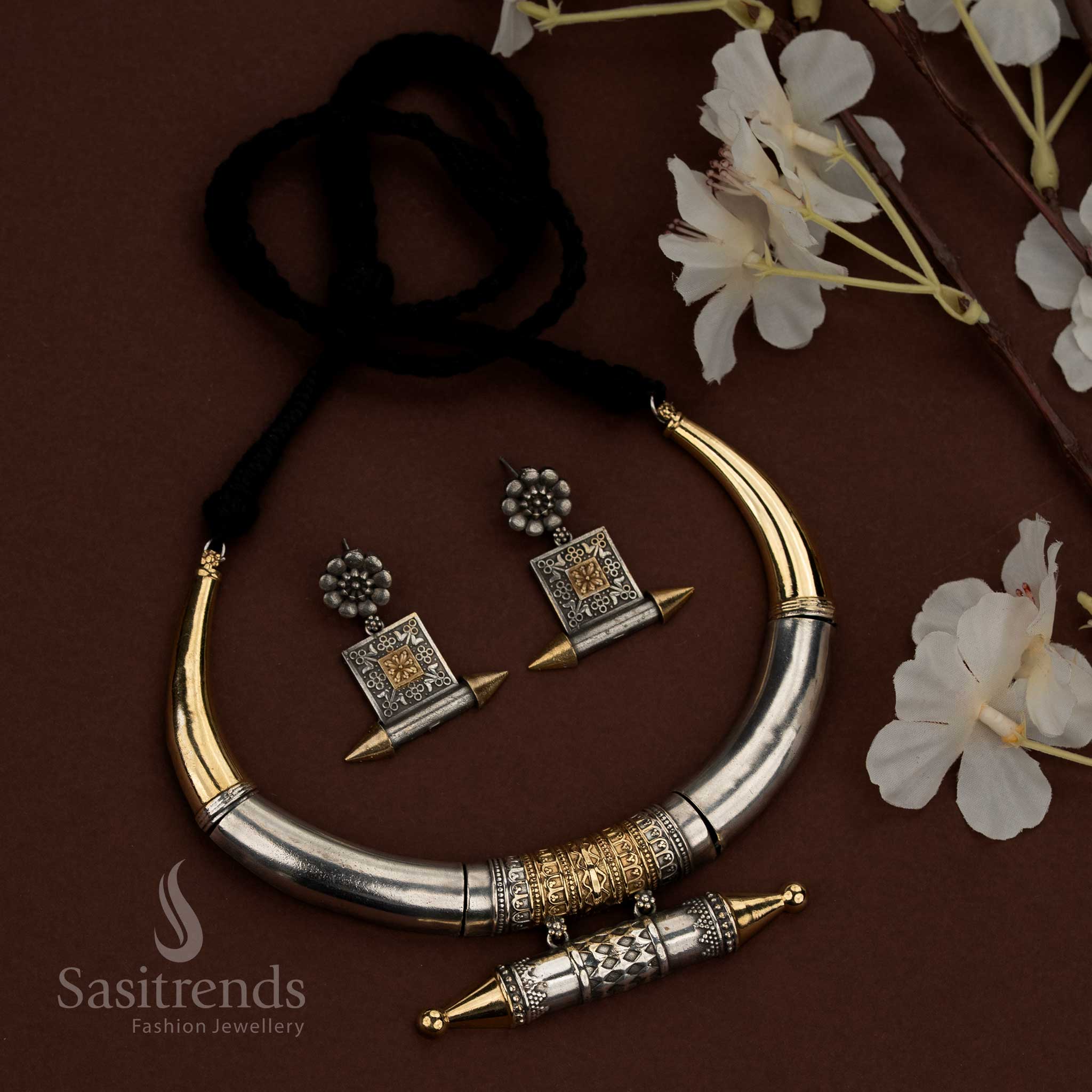 Sasitrends 92.5 dual tone silver oxidised husli necklace jewellery set featuring a bold curved crescent tubular design with smooth polished upper sections, an engraved cylindrical barrel motif at the center with repetitive geometric patterns, pointed decorative end caps, traditional thread fastening, and matching earrings designed with floral stud tops and square engraved panel drops for ethnic heritage styling.
