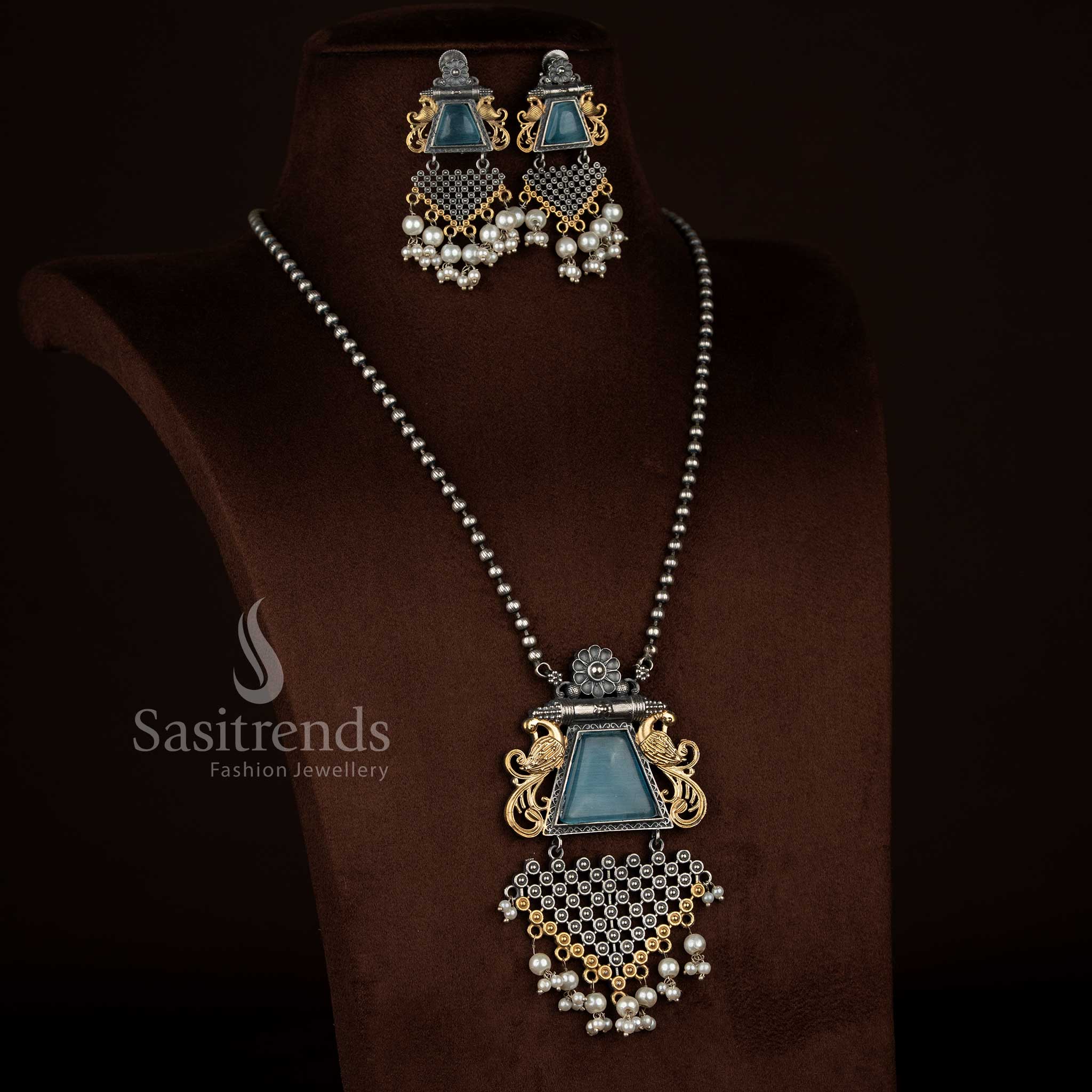 Antique oxidised 92.5 silver plated floral peacock motif pendant chain necklace set by Sasitrends designed with a sky blue Monalisa stone centerpiece, detailed floral carvings, pearl accents, textured antique finish, and matching earrings for traditional jewellery styling.
