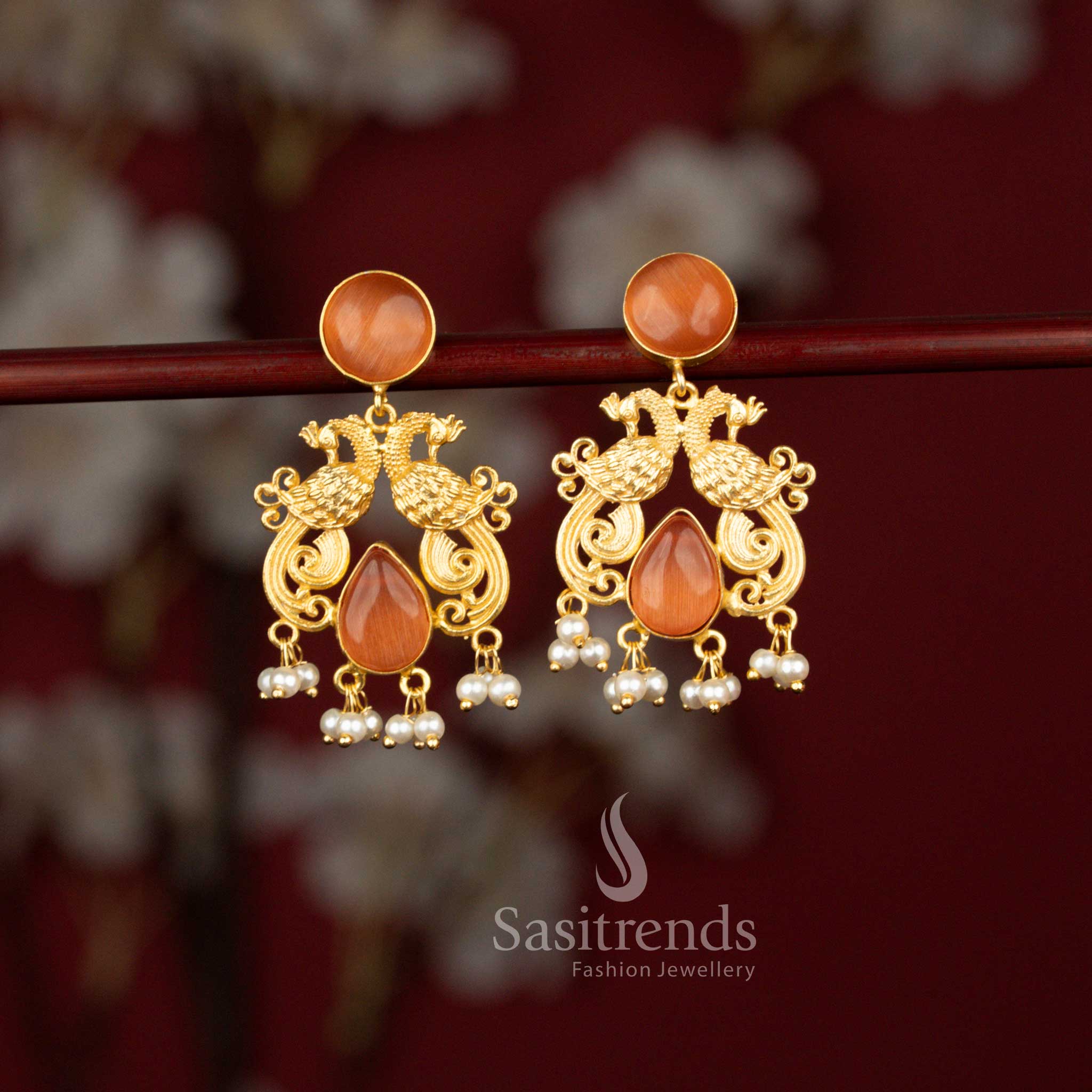 Sasitrends peach bridal inspired 24K gold plated earrings crafted with twin peacock motifs, radiant circular and teardrop stone elements and soft pearl accents for weddings and grand cultural events.