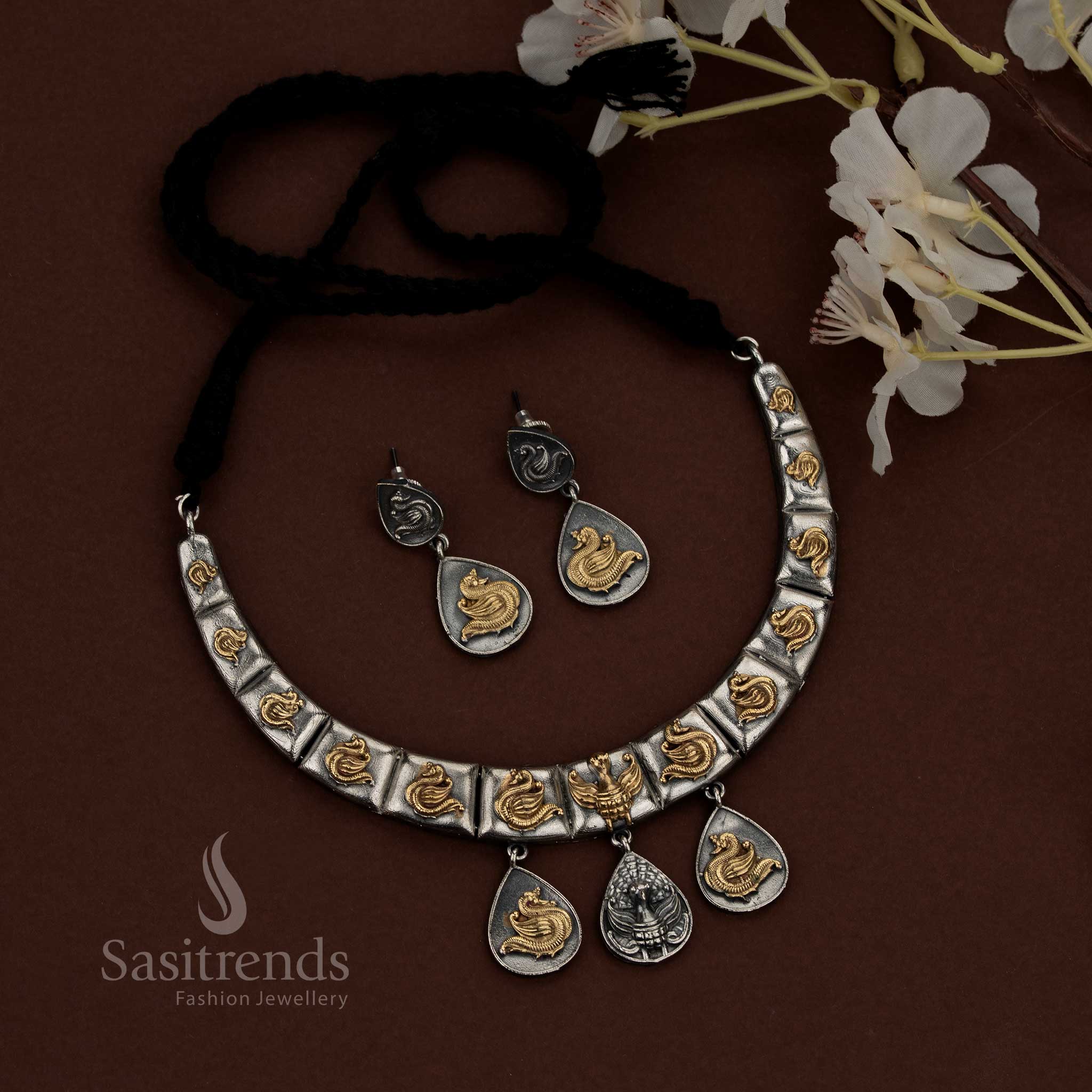 Sasitrends dual tone oxidised plated silver husli necklace set showcasing a structured segmented design with sculpted peacock motifs across each panel, oxidised surface texture with highlighted detailing, suspended teardrop danglers for depth and balance, traditional thread closure, and matching earrings reflecting the same peacock and layered design language.