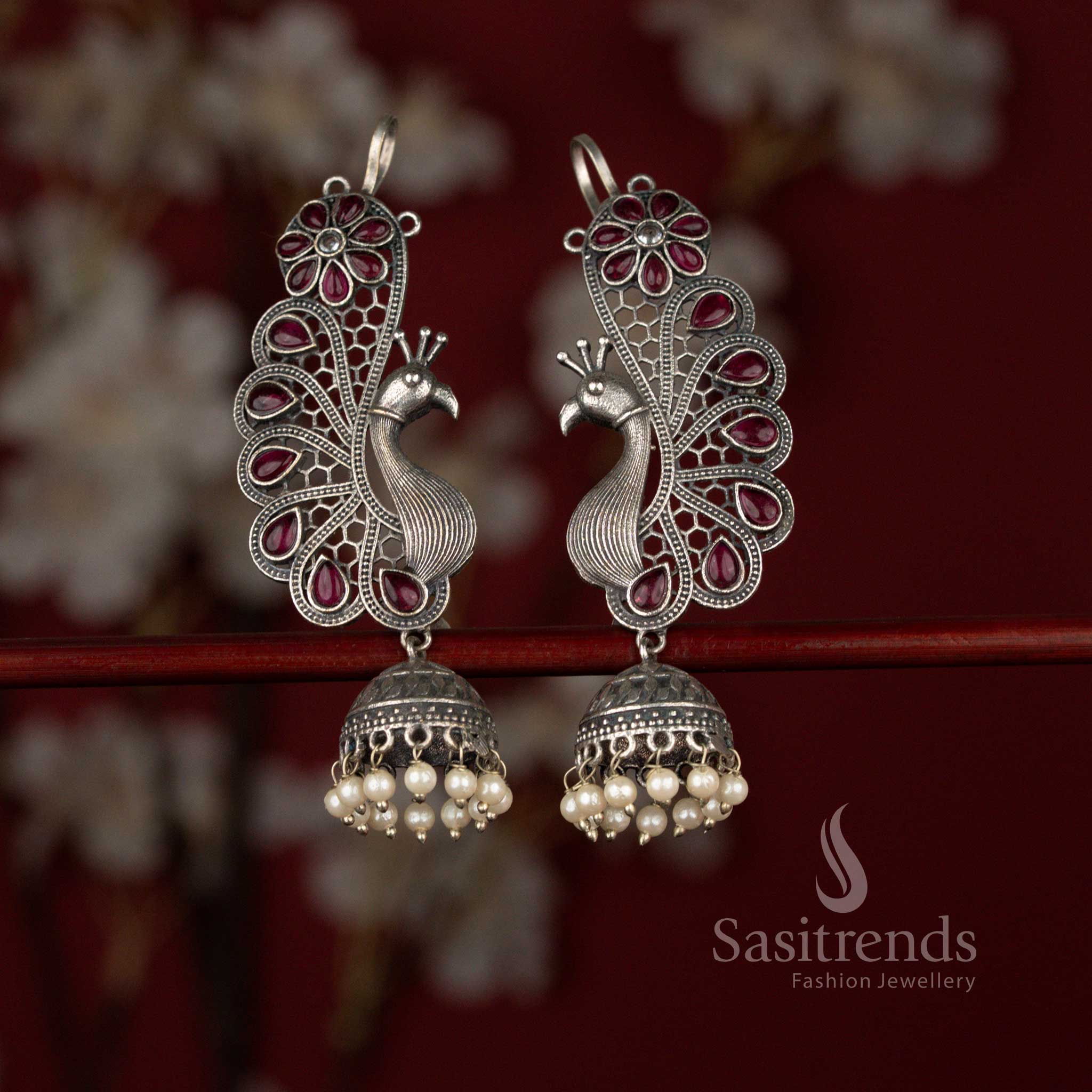 Grand ruby antique oxidised silver plated jhumka earrings from Sasitrends designed with a decorative peacock floral earcuff, radiant teardrop stone centerpiece and pearl drop finish for sarees and festive events.
