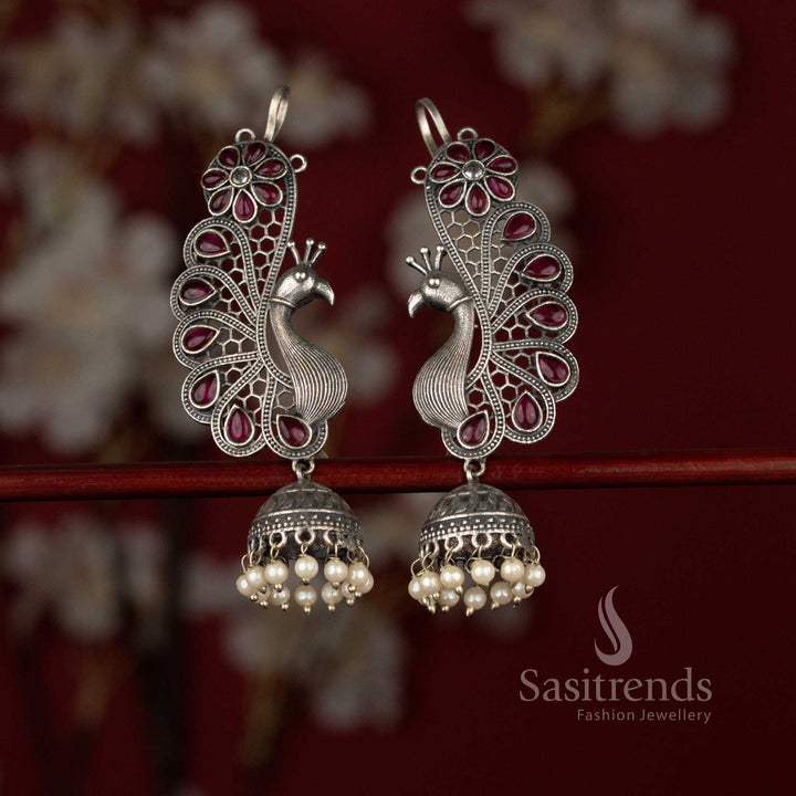 Grand ruby antique oxidised silver plated jhumka earrings from Sasitrends designed with a decorative peacock floral earcuff, radiant teardrop stone centerpiece and pearl drop finish for sarees and festive events.