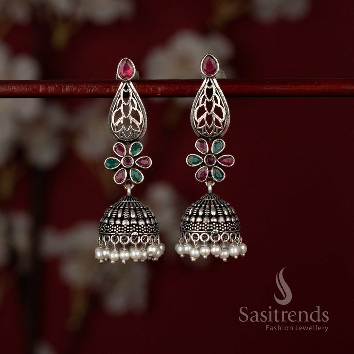 Grand oxidised German silver jhumka earrings by Sasitrends showcasing a teardrop cut ruby green Monalisa stone framed with intricate floral motifs and finished with delicate pearl drops for festive styling.
