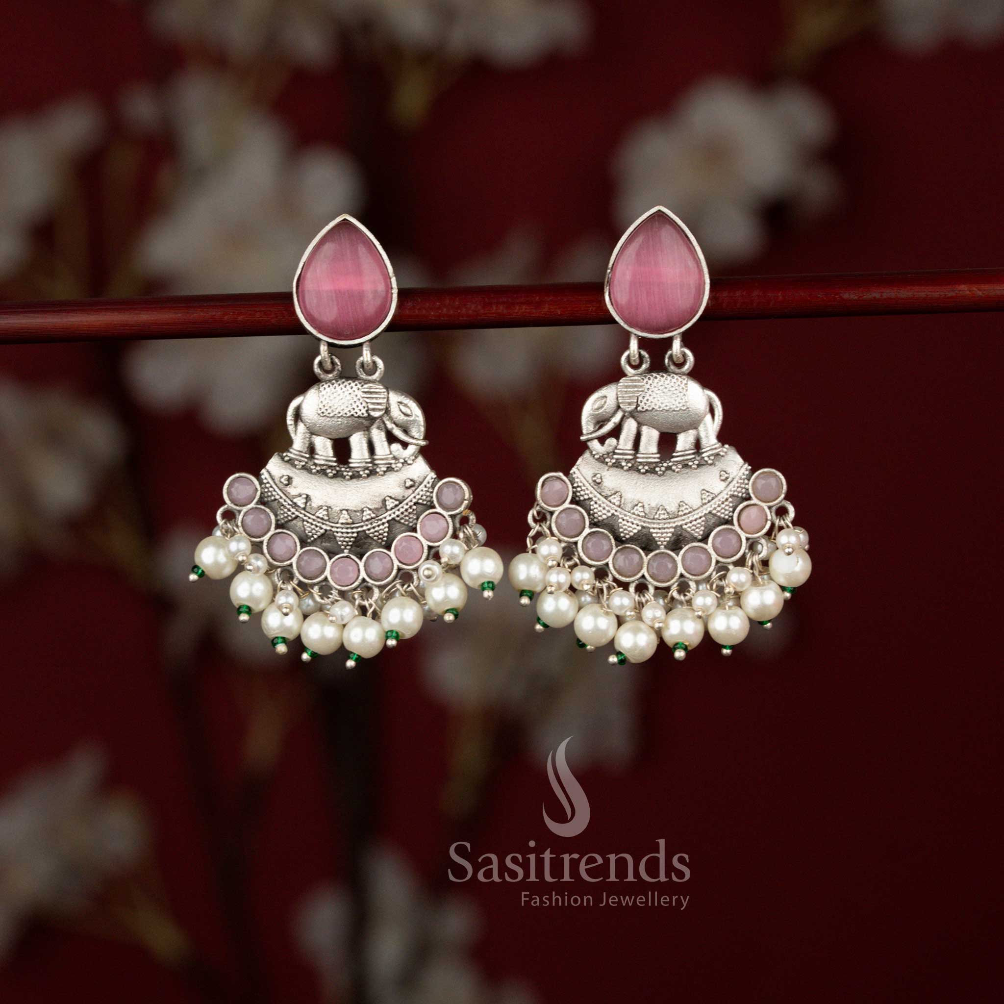 Grand Majesty pink oxidised silver earrings from Sasitrends featuring intricate elephant detailing, a bold crescent framework, shimmering teardrop stone accents and graceful pearl embellishments for festive sarees and cultural events.