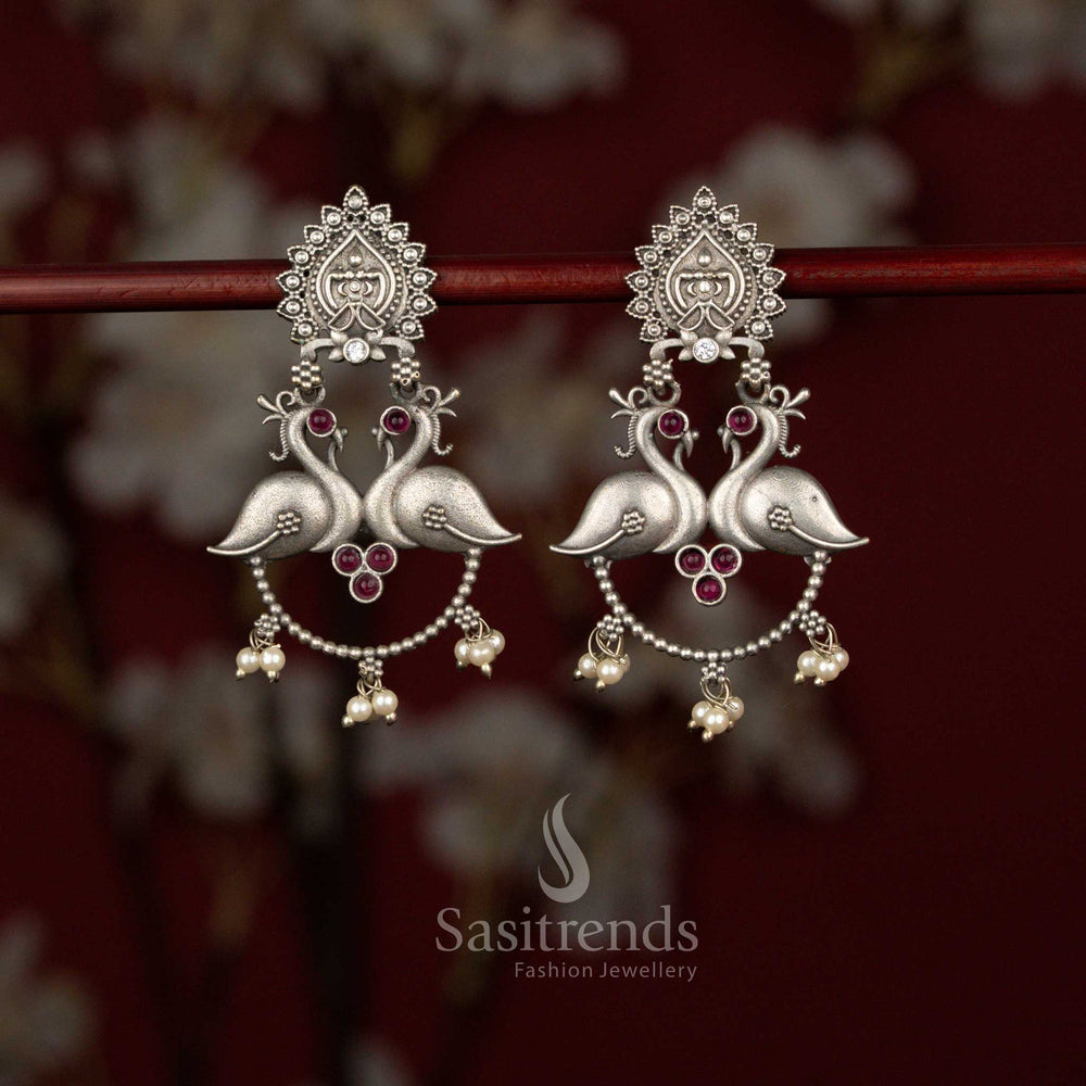 Heritage inspired ruby oxidised silver plated earrings by Sasitrends showcasing a detailed peacock motif, temple influenced stud design, artistic curved bead chains and refined pearl hangings for traditional celebrations.