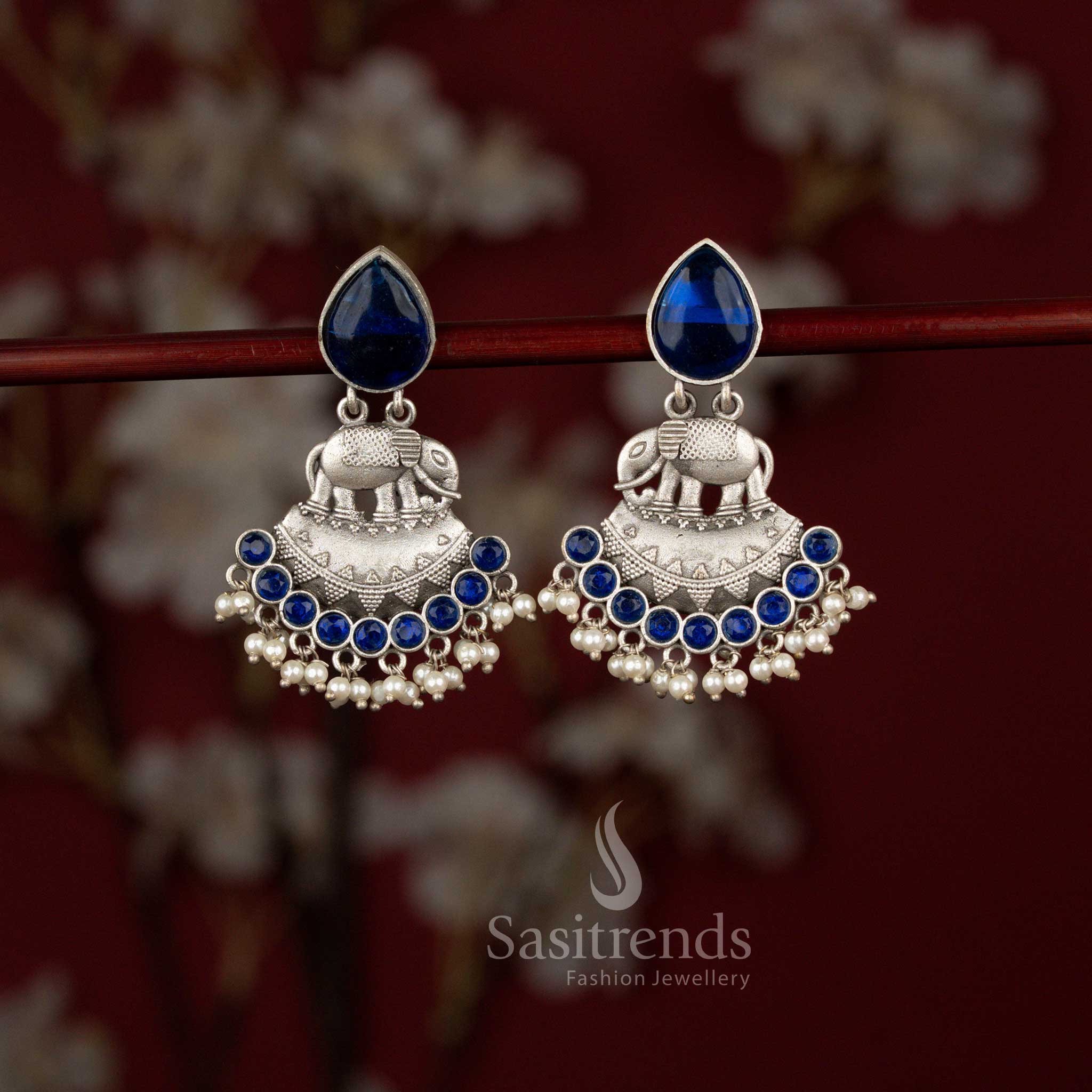 Heritage inspired blue oxidised silver Majesty earrings by Sasitrends showcasing a finely carved elephant motif, elegant crescent drop structure, highlighted teardrop stones and delicate pearl hangings for Navaratri and ethnic wear.