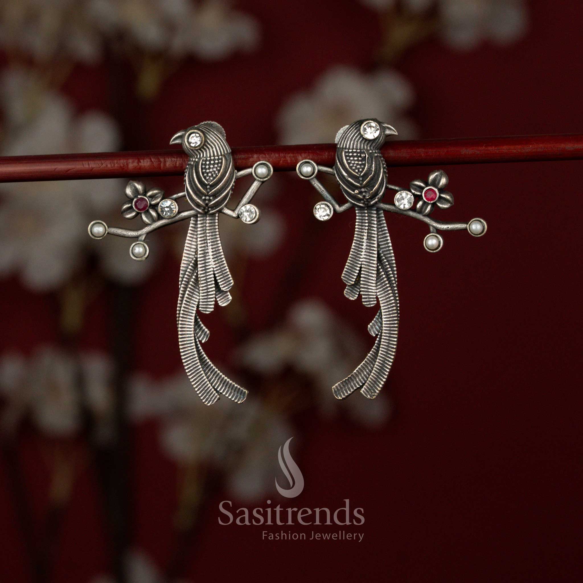 Antique style white ruby oxidised German silver earrings from Sasitrends designed with artistic twin bird motifs, intricate feather layering and a structured branch-like architectural frame for festive wear.