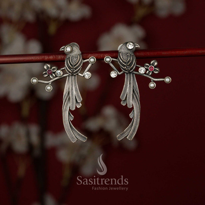 Antique style white ruby oxidised German silver earrings from Sasitrends designed with artistic twin bird motifs, intricate feather layering and a structured branch-like architectural frame for festive wear.