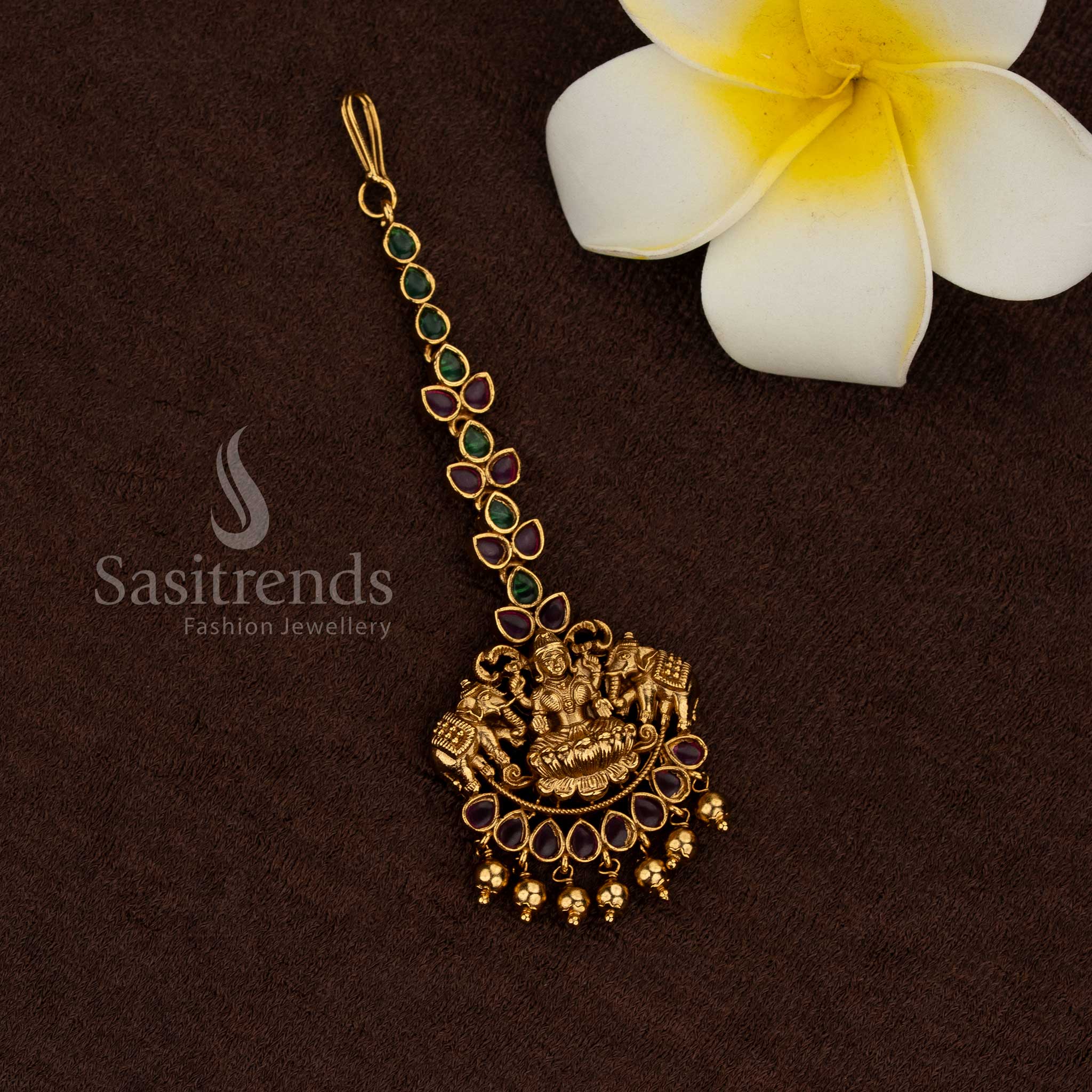 
Temple matte gold plated Lakshmi maang tikka with green and ruby stone detailing, pearl and bead drops, rich traditional premium look ideal for bridal temple wear and saree wear - Sasitrends

